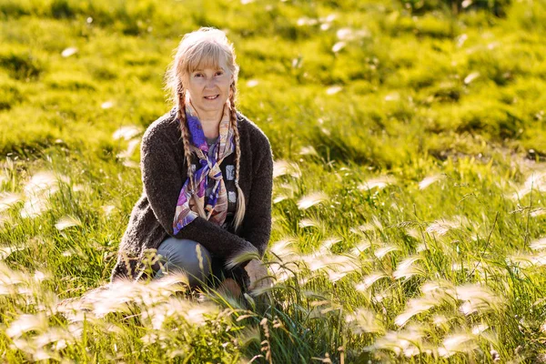 50-årig blond kvinna som sitter i gräset på sommaren — Stockfoto