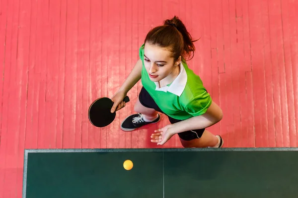 16-летняя девочка-подросток подаёт мяч в настольный теннис, вид сверху. Подростки и пинг-понг — стоковое фото