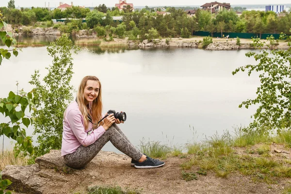 Giovane donna sorridente con macchina fotografica siede sul Lago di Shore — Foto Stock