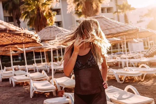 Sexig ung kvinna i transparent tunika vinka hennes långa hår i den konturformade solnedgången ljus på stranden på sommaren. — Stockfoto