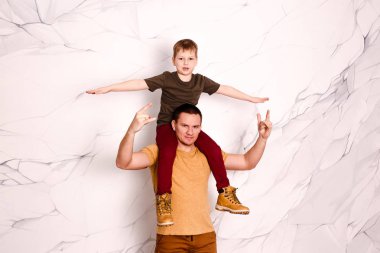 sarışın sekiz yaşında bir çocuk genç bir babanın boynuna oturur.