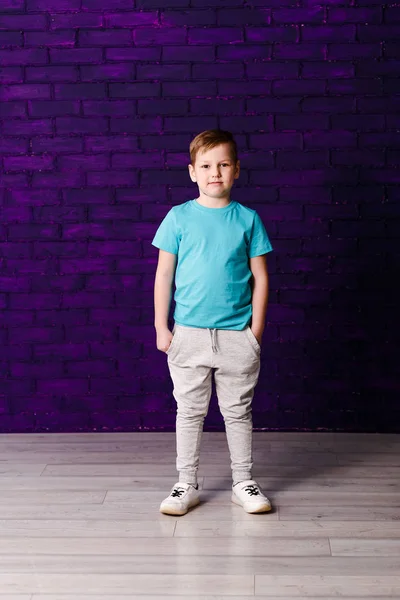Семилетний мальчик в серых штанах на фиолетовом фоне — стоковое фото