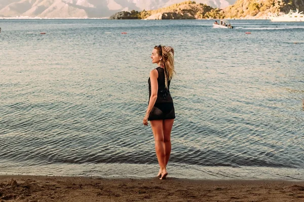 Молодая женщина в коротком платье стоит на пляже на закате — стоковое фото