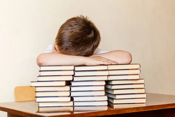 Il bambino si siede a tavola, mettendo la testa sui libri . — Foto Stock