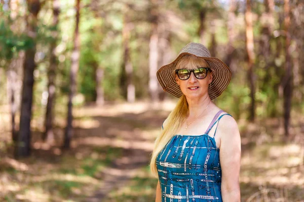 Leende 50-årig kvinna i speglade glasögon och mössa i sommar skogen — Stockfoto