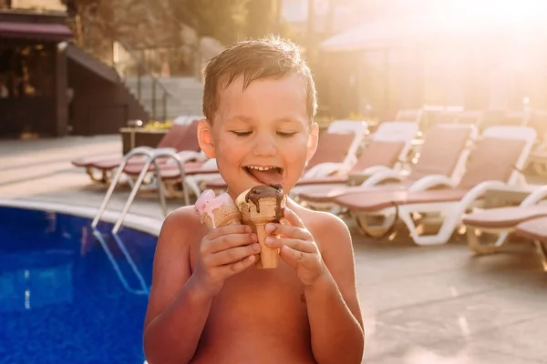five-year-old cute cheerful boy licks ice cream in the summer on vacation by the pool.