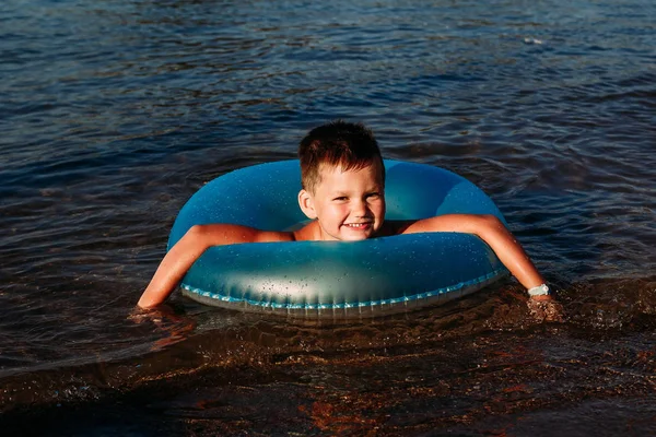 Χαρούμενο παιδί κολυμπάει στη θάλασσα με ένα μπλε καουτσούκ κύκλο — Φωτογραφία Αρχείου