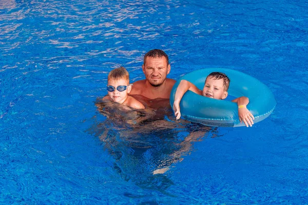 Ευτυχισμένος μαυρισμένος άνθρωπος με δύο παιδιά κολύμπι σε μπλε εξωτερική πισίνα — Φωτογραφία Αρχείου