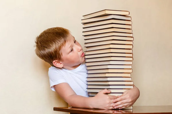 Un bambino di otto anni guarda una grande pila di libri. persone e libri . — Foto Stock