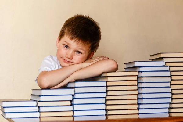 Улыбающийся шестилетний мальчик, сидящий за столом с руками на книгах — стоковое фото