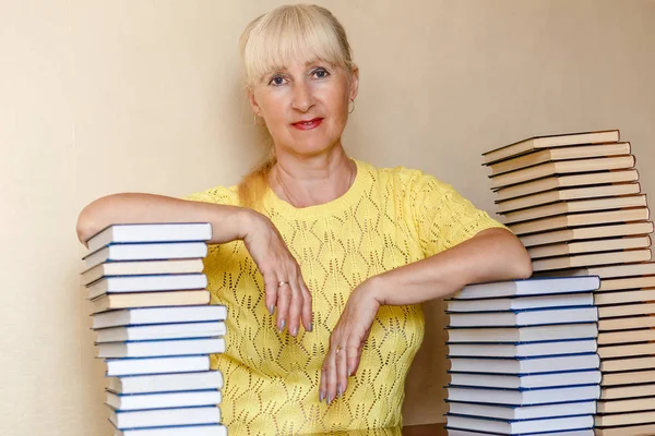 Пятидесятилетняя женщина в желтом свитере сидит за столом с книгами — стоковое фото
