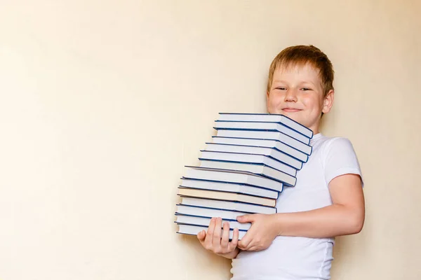 Osiem lat uśmiechnięty chłopiec trzyma wiele książek. pierwszy równiarka — Zdjęcie stockowe