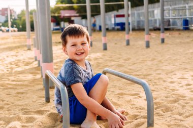 Sahilde sarı kum üzerinde oturan beş yaşındaki çocuk gülümseyen