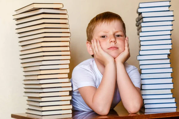 Smutny ośmioletni chłopiec i wiele książek na stole — Zdjęcie stockowe