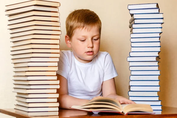 eight-year-old Caucasian boy in a white t-shirt reading a book , sitting at the table