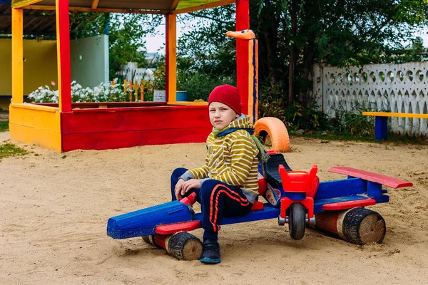 Garçon caucasien de sept ans jouant sur le terrain de jeu à la maternelle. Enfant assis sur une voiture jouet en bois — Photo