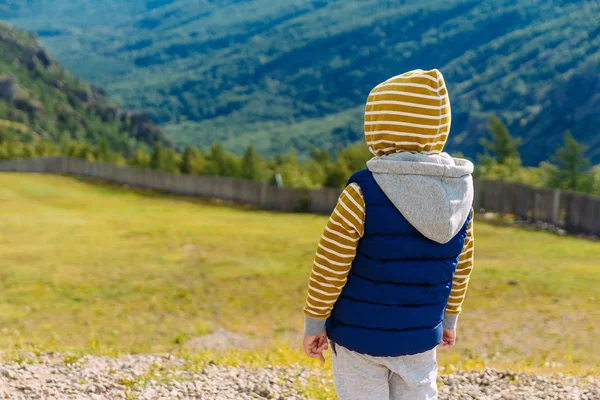 Шестилетний мальчик в теплой одежде стоит спиной на фоне красивого горного пейзажа — стоковое фото