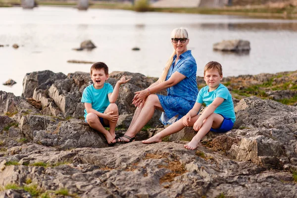 A young grandmother and two grandchildren sit — Stock Photo, Image