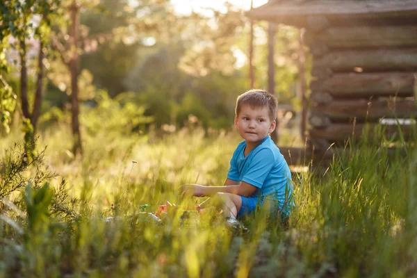 Кавказский коротковолосый пятилетний мальчик, сидящий в высокой траве в саду летом — стоковое фото