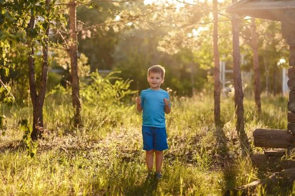 Deportivo niño caucásico de cinco años de edad en camiseta azul y pantalones cortos se encuentra en la luz del sol trasera en verano al aire libre —  Fotos de Stock