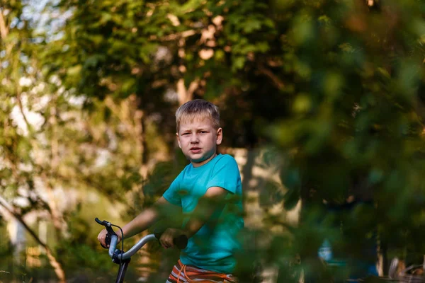 Serious seven year old boy Cycling through leaves on blurred natural background — Stock Photo, Image