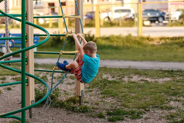 Семилетний мальчик в шортах поднимается летом на игровую площадку — стоковое фото
