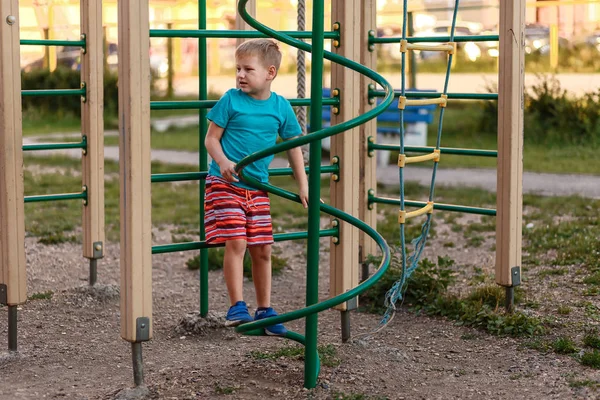Семилетний спортивный мальчик в шортах играет летом на детской площадке — стоковое фото