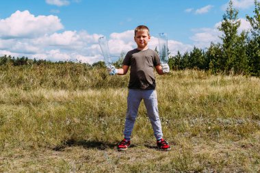 çalışan eldiven ciddi sekiz yaşındaki çocuk plastik çöp kaldırır , boş plastik şişe gösterir.