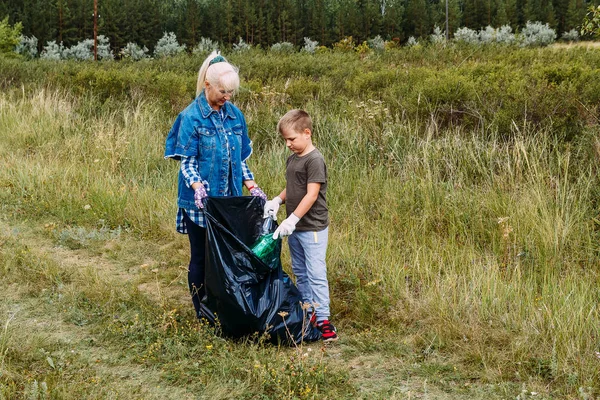boy and grandma put empty plastic bottles in a big black garbage bag