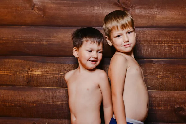 Два смешных коричневых мальчика дошкольника стоят друг перед другом на заднем плане деревянной стены . — стоковое фото