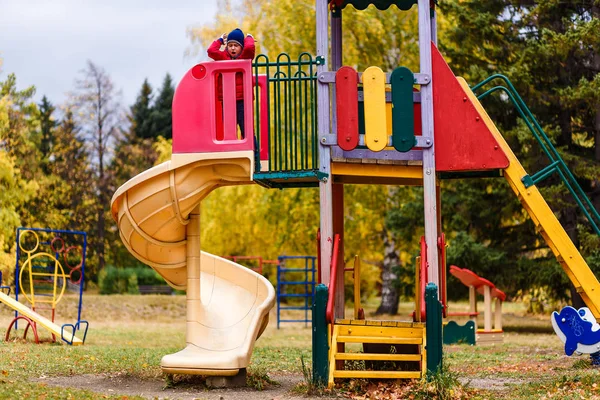 Un enfant dans une veste chaude et un chapeau jouant sur l'aire de jeux extérieure — Photo