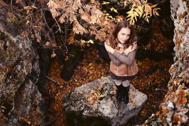 Sonbaharda ağaçların arasındaki bir kayada duran üzgün genç bir kadın..