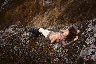 Genç beyaz kadın sonbaharda dağlarda bir kayanın üzerinde yatıyor.