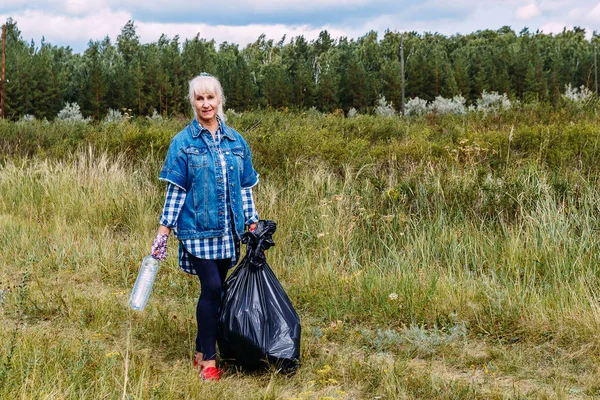 Женщина пенсионного возраста в рабочих перчатках вывозит пластиковый мусор — стоковое фото
