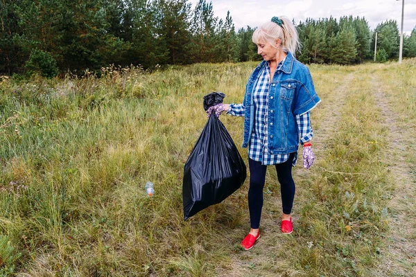 Женщина пенсионного возраста в рабочих перчатках вывозит пластиковый мусор в мешке — стоковое фото