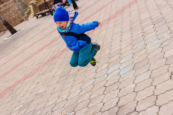 five-year-old boy in blue cap jumps high over rope