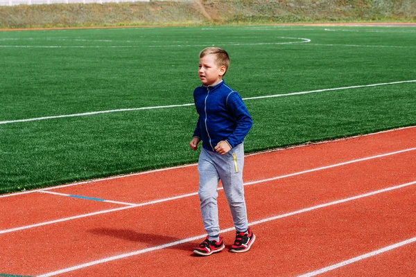 Ragazzo caucasico di otto anni in scarpe da ginnastica rosse corre attraverso uno stadio sportivo — Foto Stock