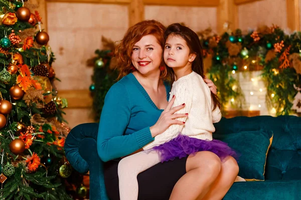 En sexårig flicka med mörkt hår sitter i mammas knä i julrummet. mor och dotter — Stockfoto