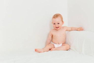 10 aylık, bebek beziyle gülümseyen bir bebek yatakta oturuyor.