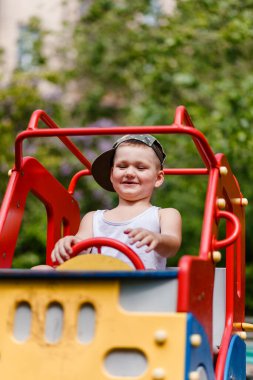 Neşeli bir çocuk yazın parkta bir çocuk arabasının direksiyonunu çevirir. dikey resim