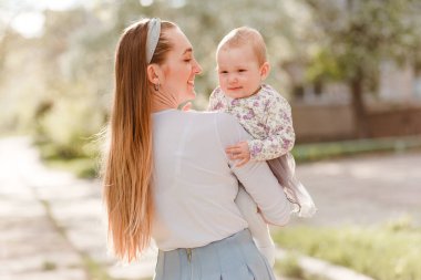 Genç bir anne on aylık şirin bir bebeği kollarında tutuyor. Uzun yaz saçlı bir kadın.