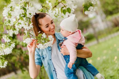 Gülümseyen mutlu genç anne küçük kızı kollarına aldı ve çiçeklerini açtı.