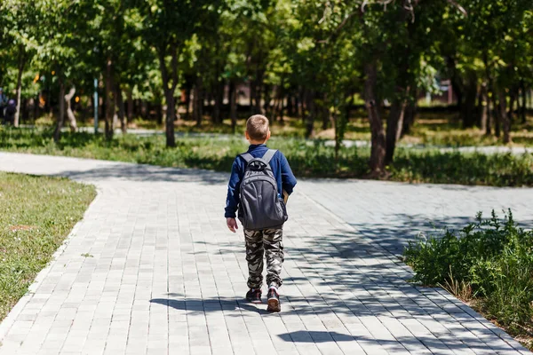 A schoolboy with a large backpack on his back walks along a path in the park. photo with back