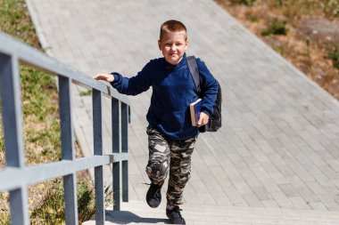 Sekiz yaşında mutlu bir çocuk merdivenlerde okula yürür. Okula dönüyorum. Sırtında kitap ve sırt çantası olan bir bebek.