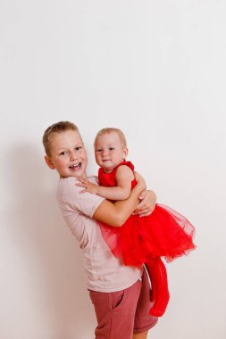 8 yaşında bir oğlan, beyaz arka planda küçük bir kızı tutuyor.