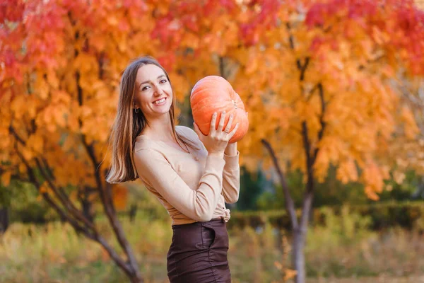 smiling young woman with pumpkin in her hands on a blury autumn background
