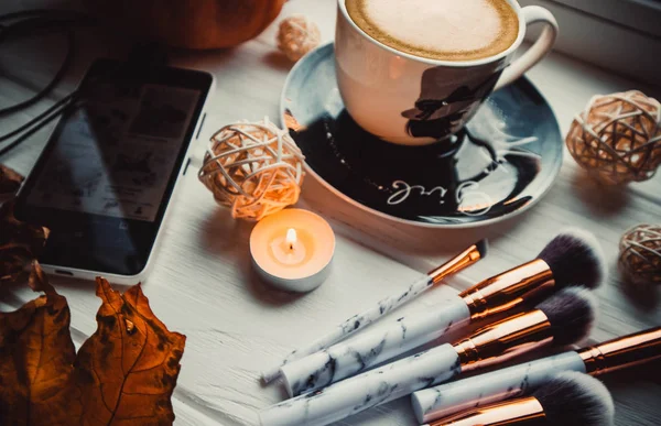 Stylish flatlay arrangement with coffee, brushes, candles, phone and other stationary accessories.