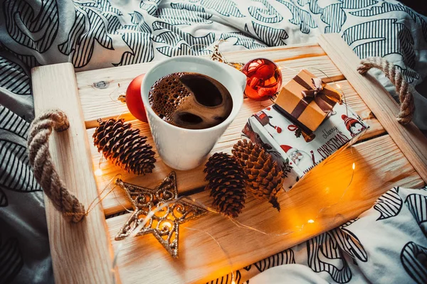 Tahta tepside bir fincan kahve ve Noel oyuncakları.