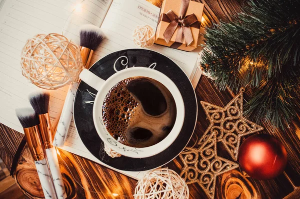 Ahşap arka planda bir fincan kahve Noel oyuncakları ve not defteriyle