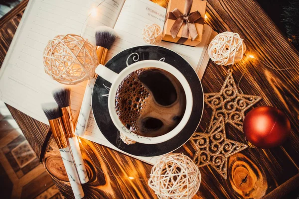 Ahşap arka planda bir fincan kahve Noel oyuncakları ve not defteriyle